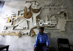 A security guard sits in front of a wall with signs and slogans at the operation building at the Pakistan Steel Mills on the outskirts of Karachi