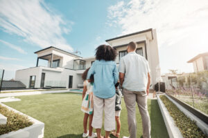 Love, new house and family in their backyard together looking at their property or luxury real estate. Embrace, mortgage and parents with their children on grass at their home or mansion in Canada.