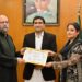 Senior Pakistani artist Aliya Faizi receiving a Certificate of Appreciation at the FPCCI Lifestyle Committee exhibition alongside organisers and guests.