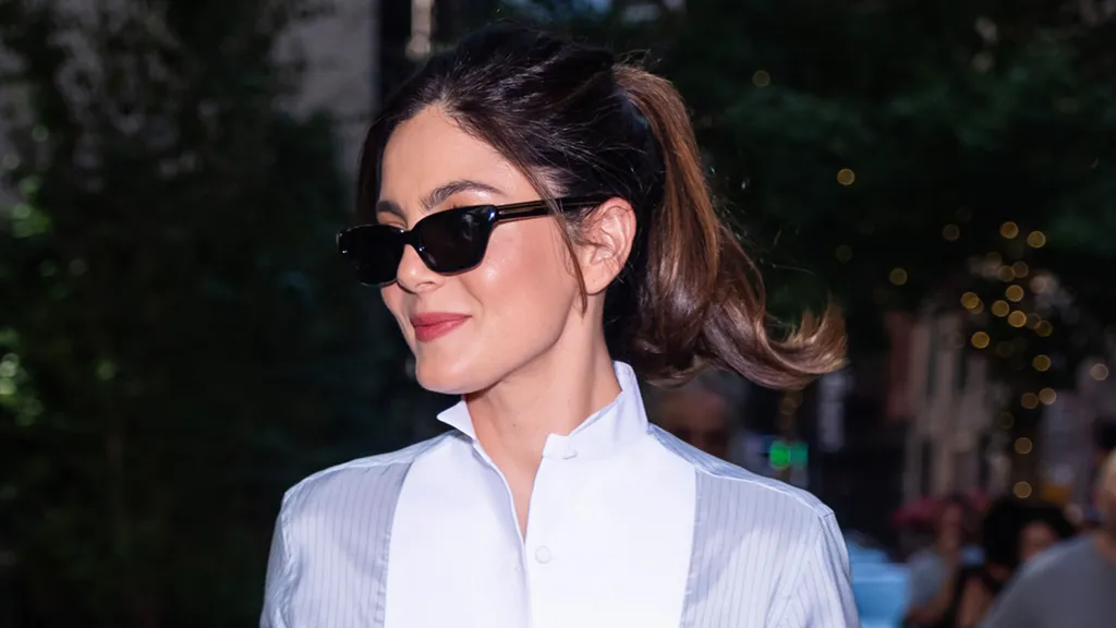 Monica Barbaro styling a blue-and-white tuxedo shirt with black tailored trousers and pumps